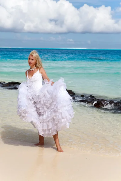 A bela mulher jovem em um vestido da noiva que está na borda do mar — Fotografia de Stock