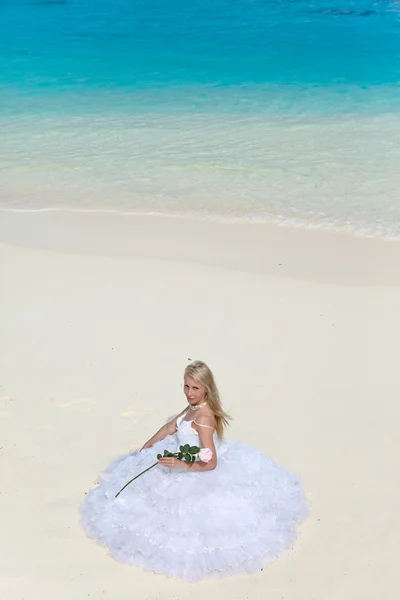 Mladá krásná žena v šatech nevěsty sedí na písku na okraji moře — Stock fotografie
