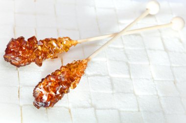 Candy brown sugar on a stick lies on white lumpy sugar clipart