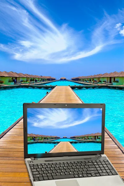 Wooden road to small houses over the sea and the laptop with a beach pictur — Stock Photo, Image