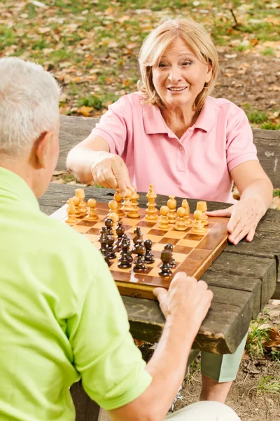 Feliz casal sênior jogar xadrez em um banco de parque — Fotografia de Stock