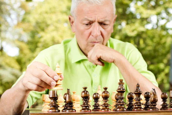 Портрет обеспокоенного пожилого человека, играющего в шахматы на открытом воздухе — стоковое фото