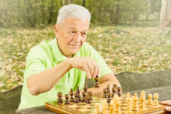 Starszy mężczyzna gra w szachy w parku — Zdjęcie stockowe