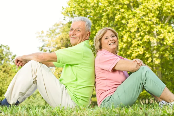 Счастливая пожилая пара сидит на траве — стоковое фото
