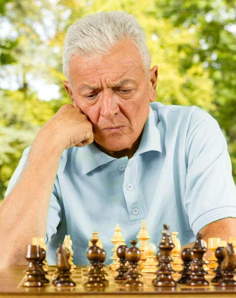 Portrait of worried elderly man playing chess outdoors