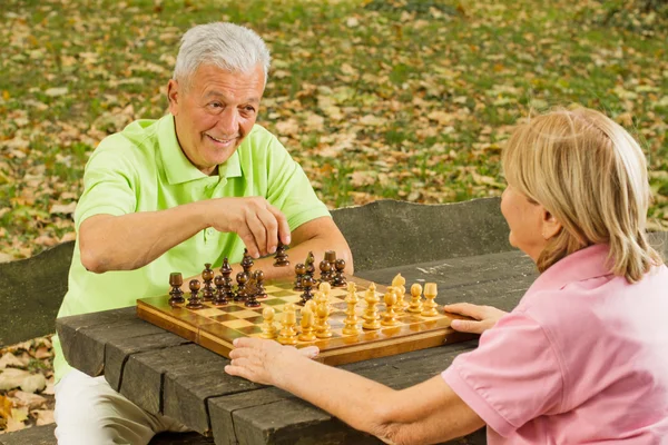 Счастливая старшая пара играет в шахматы на скамейке в парке — стоковое фото