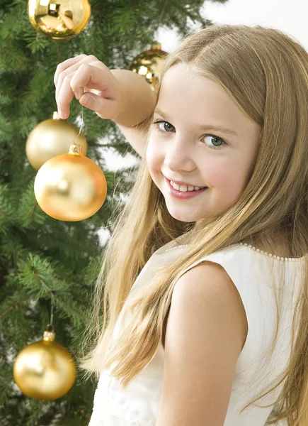 Smiling girl with christmas balls next to green tree — Stock Photo, Image