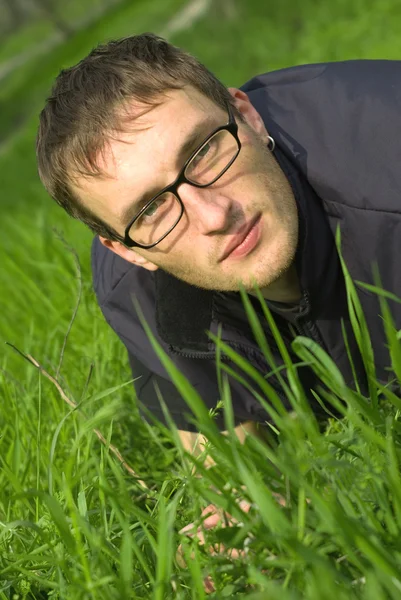 Young man in glasses is liyng in green grass — Stock Photo, Image