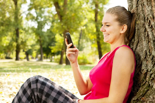 Vrouw met mobiele telefoon in park — Stockfoto