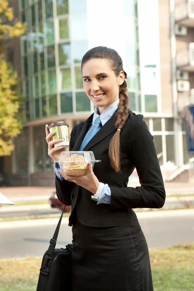 Mujer de negocios sonriente con desayuno en las manos — Foto de Stock
