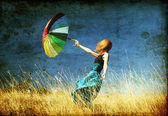 rothaarige Mädchen mit Regenschirm auf windiger Graswiese.