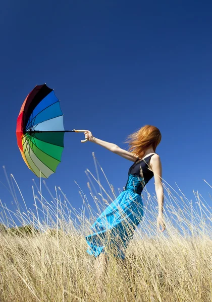 Roodharige meisje met paraplu op winderige gras weide. — Stockfoto