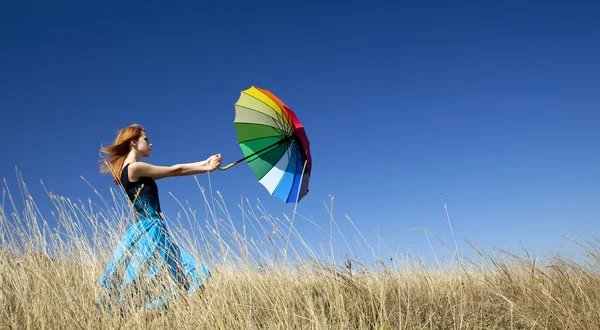 Rusovláska dívka s deštníkem na louce větrno trávy. — Stock fotografie