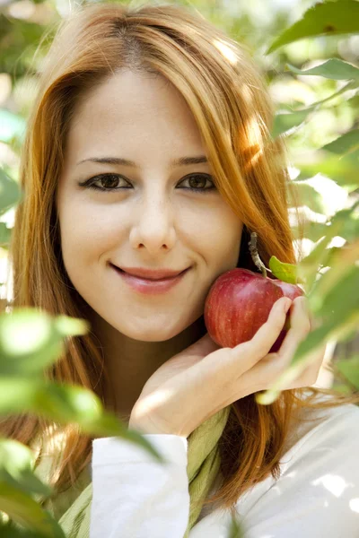 Schöne junge rothaarige Frau, die neben dem Apfelbaum steht. — Stockfoto