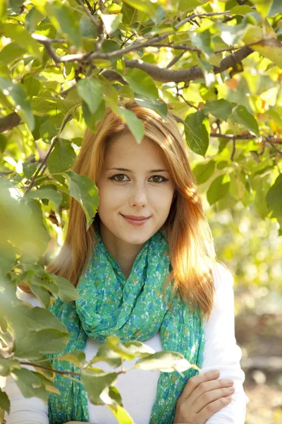 Schöne junge rothaarige Frau, die neben dem Apfelbaum steht. — Stockfoto