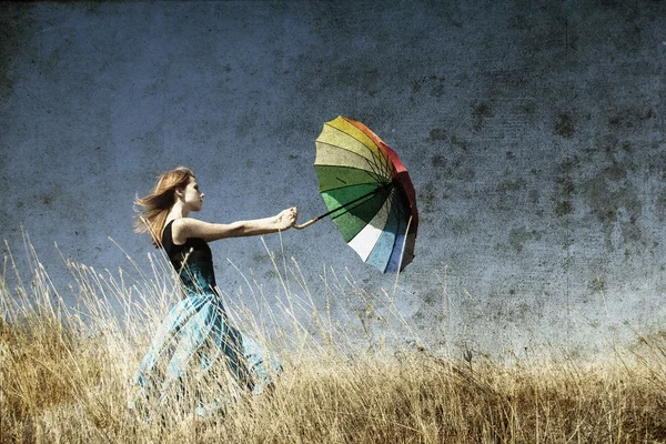 Rusovláska dívka s deštníkem na louce větrno trávy. — Stock fotografie