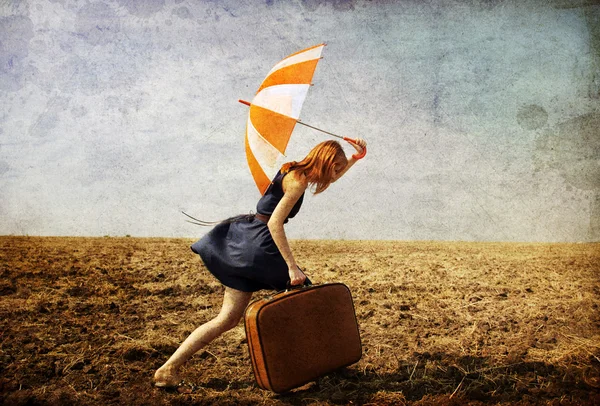 stock image Lonely girl with suitcase and umbrella at countryside field.