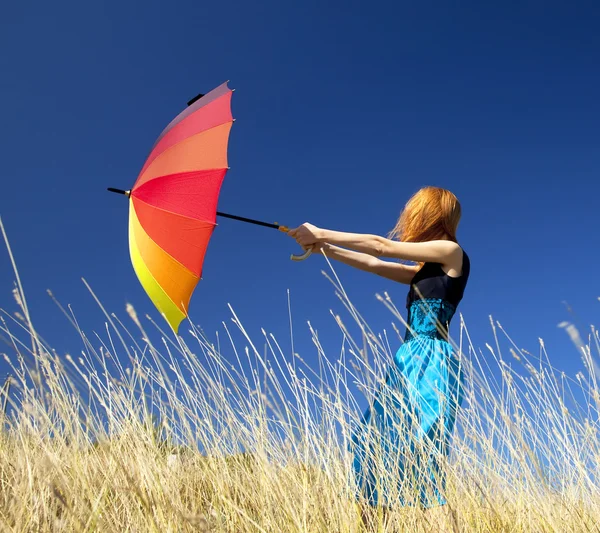 Rödhårig tjej med paraply på blåsiga gräs äng. — Stockfoto