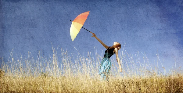 Roodharige meisje met paraplu op winderige gras weide. — Stockfoto