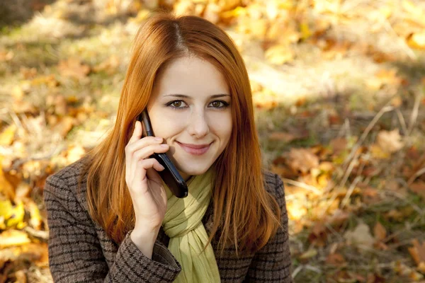 Rusovlasá dívka volá telefonicky v podzimním parku. — Stock fotografie