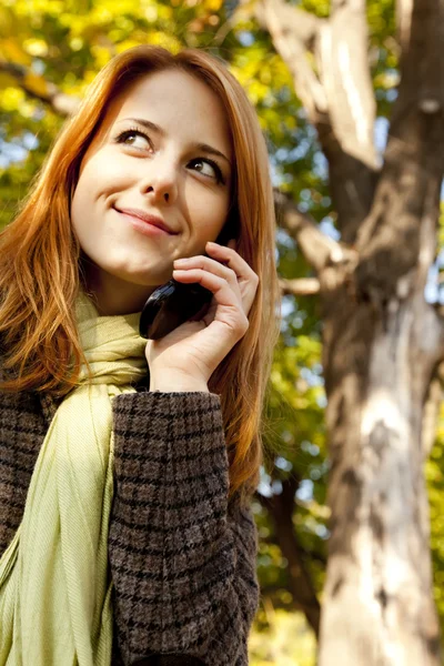 Рыжая девушка звонит по телефону в осеннем парке . — стоковое фото