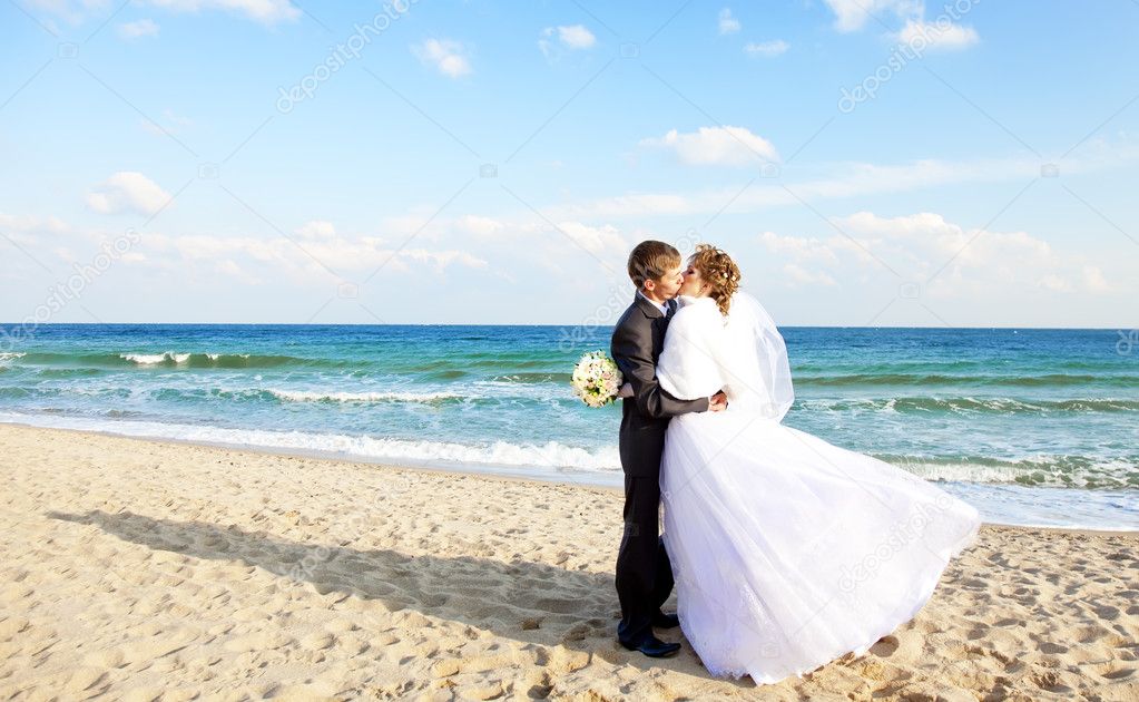 Newly married couple kissing on the beach.
