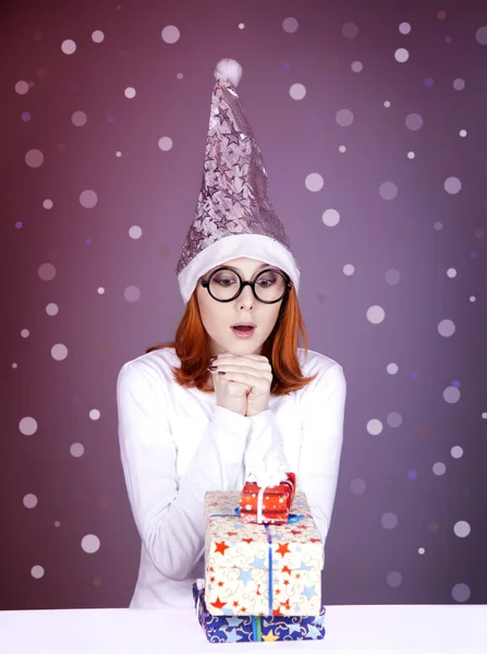 Funny red-haired girl in christmas cap with gift boxes. — Stock Photo, Image