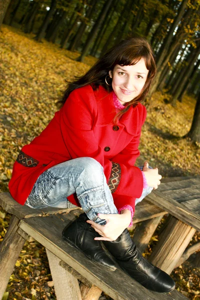La belle femme en manteau rouge sur un banc avec le grand sourire — Photo