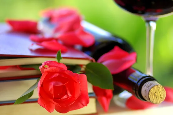 Pétalas de rosa vermelha em livros e garrafa de vinho . — Fotografia de Stock