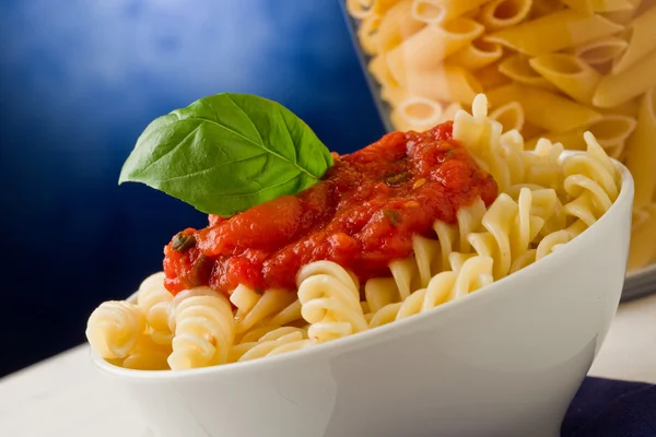 Nudeln mit Tomatensauce und Basilikum auf blauem Hintergrund — Stockfoto