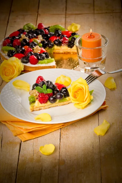 Пирог с фруктами и лепестками, освещенный свечой — стоковое фото
