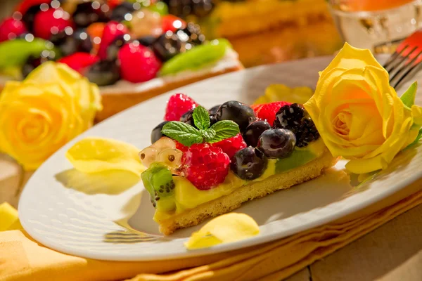 Kuchen mit Früchten und Blütenblättern im Kerzenschein — Stockfoto