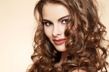 Lovely model with shiny volume curly hair. Pin-up style on beige background
