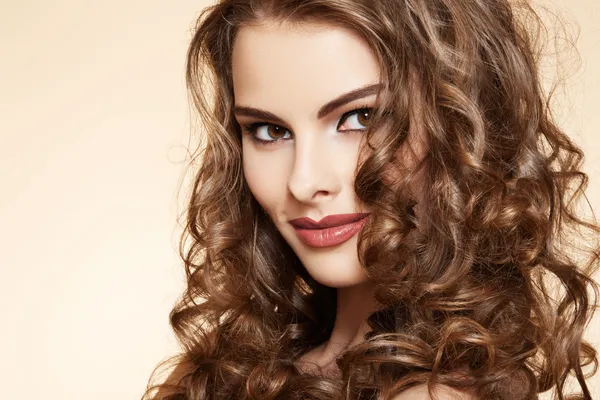 Schönes Modell mit glänzendem Volumen lockigem Haar. Pin-up-Stil auf beigem Hintergrund lizenzfreie Stockfotos