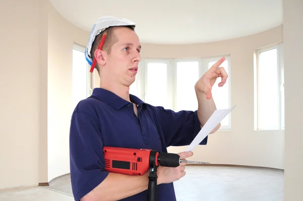 Giovane uomo serio con trapano e cappello di carta in nuovo edificio — Foto Stock