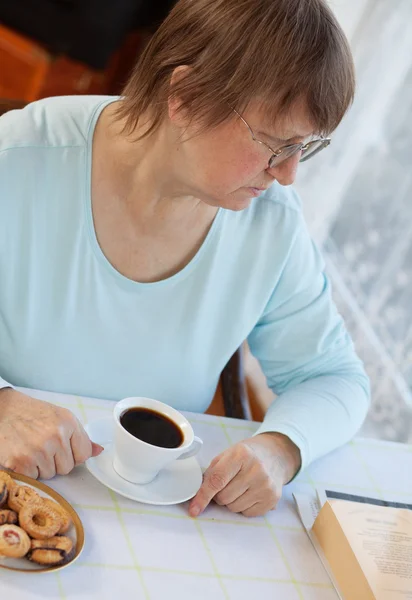 Oudere vrouw met koffie met cookies — Stockfoto