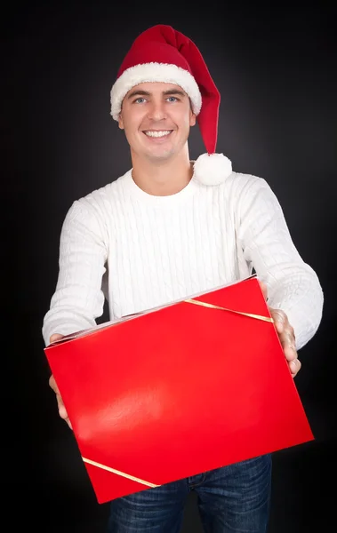 Улыбающийся человек в шляпе Санты дает красную коробку в студии — стоковое фото