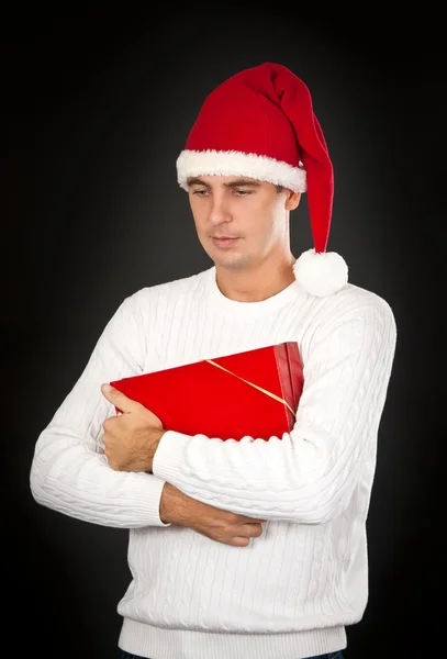 Homem triste em um chapéu Papai Noel com um presente — Fotografia de Stock