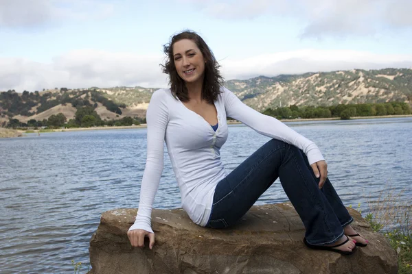 Junge kaukasische Frau sitzt auf einem Felsen am See — Stockfoto