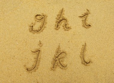 Alphabet letters handwritten in sand on beach clipart