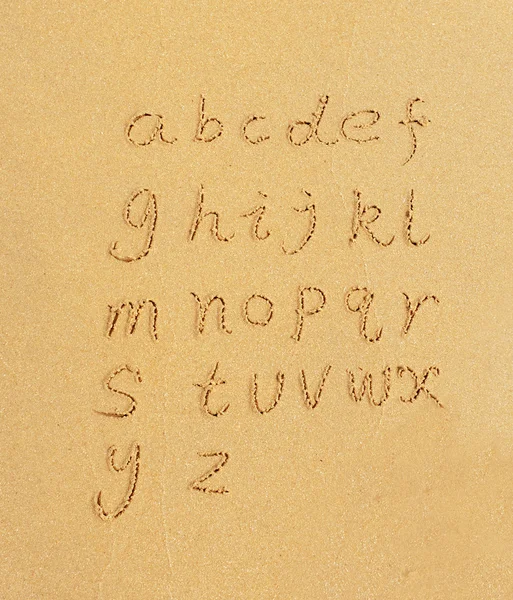 Алфавитные буквы, написанные от руки песком на пляже — стоковое фото