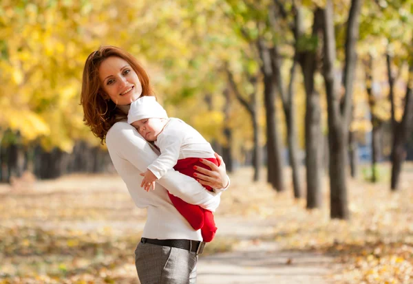 Young mother with sleeping child on hands in autumn park — Stock Photo, Image