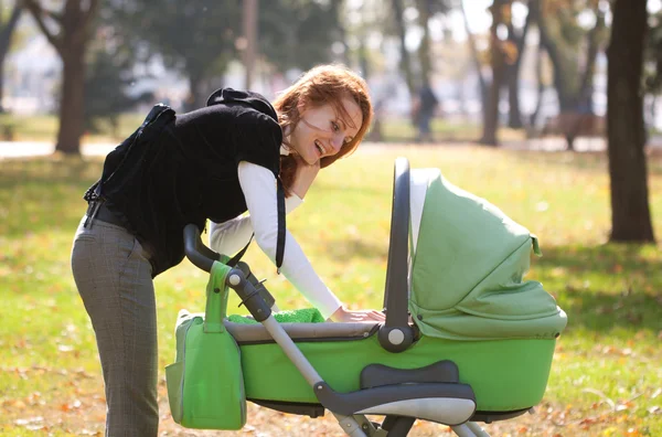 Genç anne bebek sonbahar park içinde taşıma — Stok fotoğraf