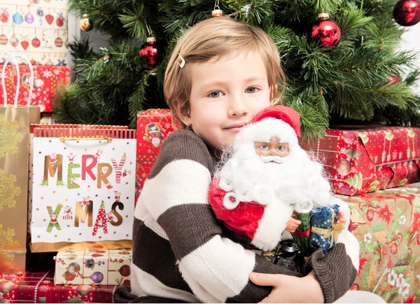 Criança com boneca de Papai Noel na frente da árvore de natal — Fotografia de Stock