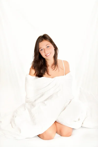 Beautiful young woman sitting on white bed — Stock Photo, Image
