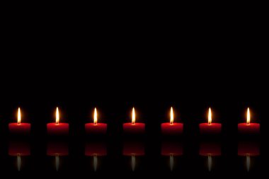 Burning red candles in front of black background clipart
