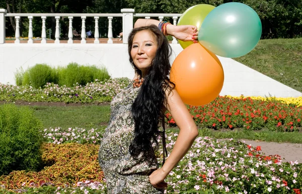 Радостная беременная девушка с красочными воздушными шарами гуляет в парке — стоковое фото