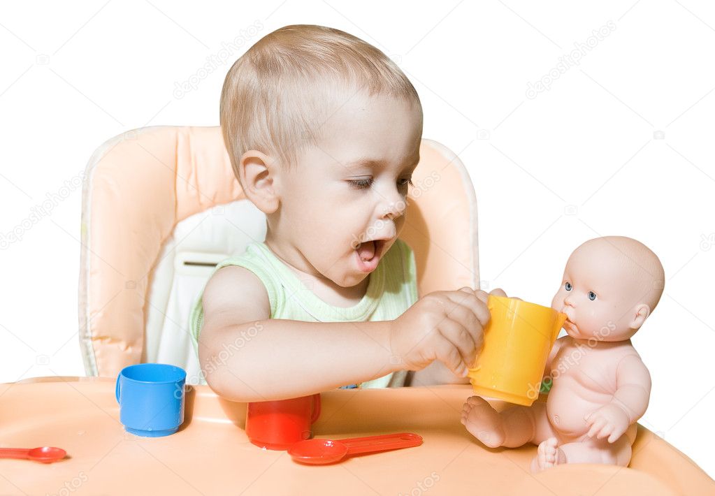Adorable child independently feeding doll sitting in front of th