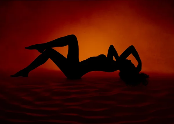 Žena sexy siluetou ležící v červené oranžové pozadí — Stock fotografie