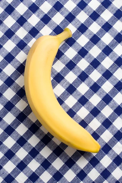 Yellow banana on checkered tablecloth — Stock Photo, Image